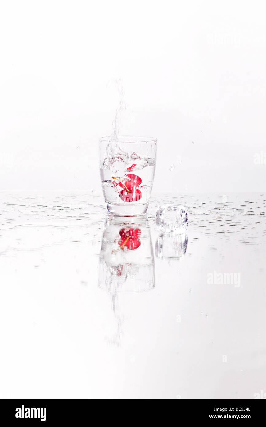 Cocktail cherry falling into a water glass with ice cubes Stock Photo
