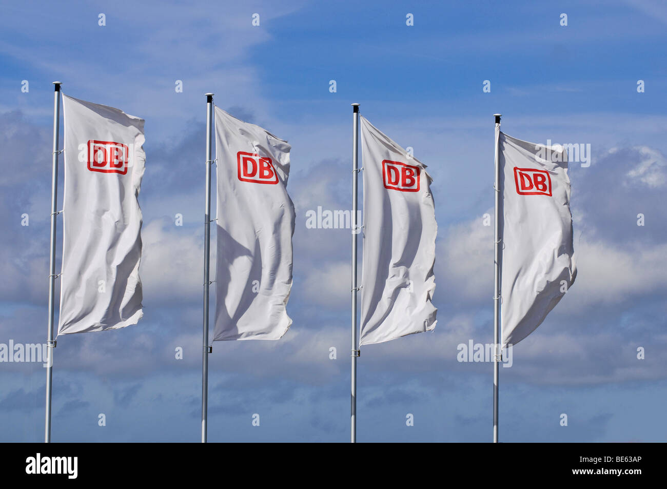 Four windblown white flags with the logo of DB, German Railways, in front of a sunny sky Stock Photo