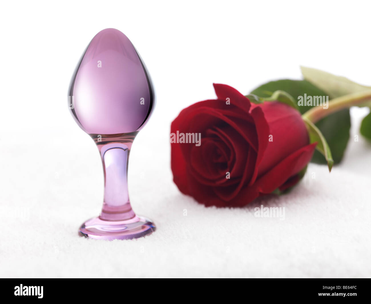 Glass dildo Sex toy and a red rose on a white towel Stock Photo