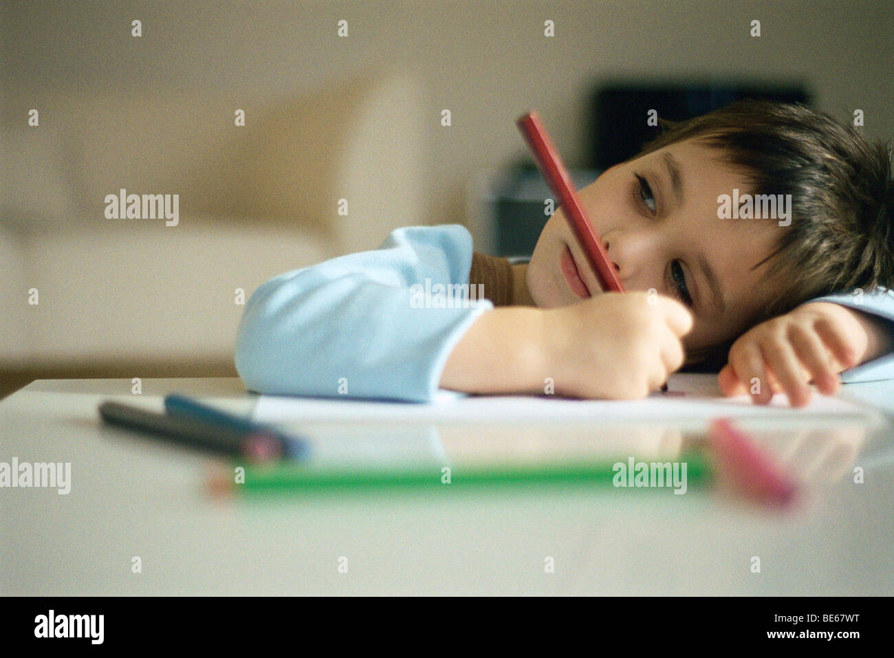 Little boy pausing while drawing, resting head on arm Stock Photo