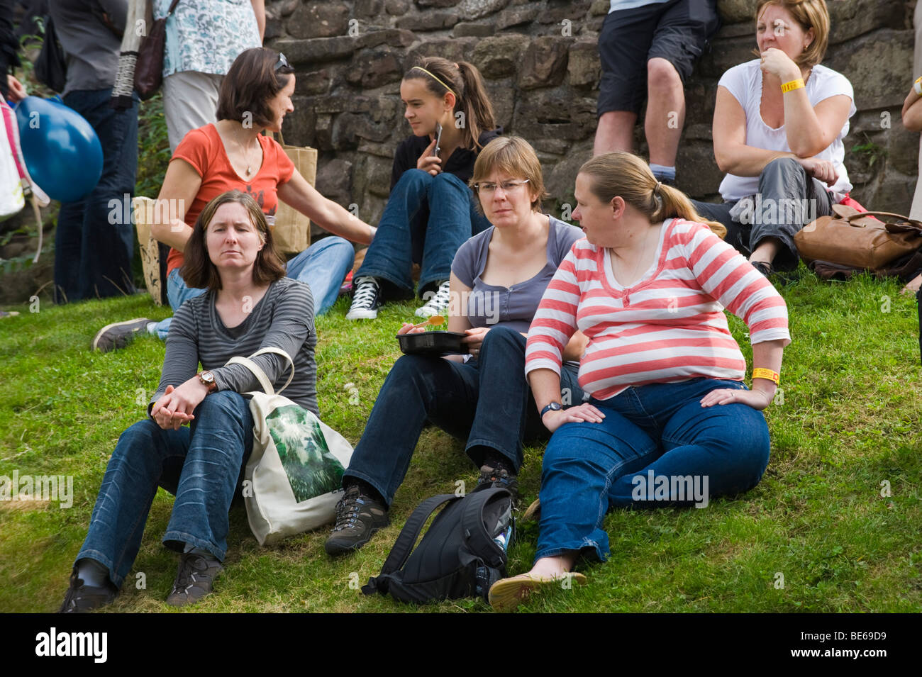 Women eating snacks on grassy bank in castle grounds during Abergavenny Food Festival Monmouthshire South Wales UK Stock Photo