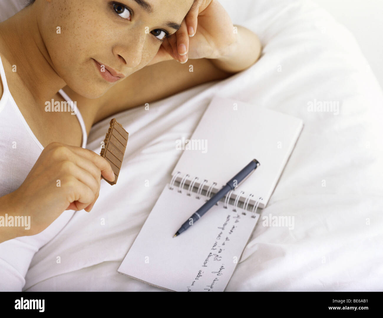 Young woman eating chocolate and writing in diary Stock Photo