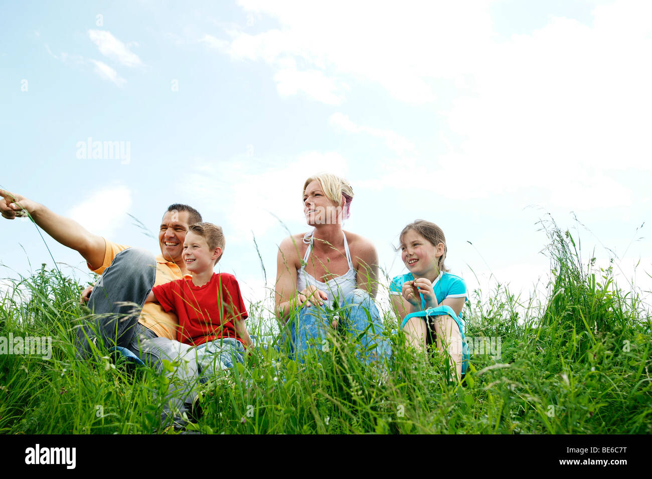 Familiy sitting on a meadow, looking into the distance Stock Photo