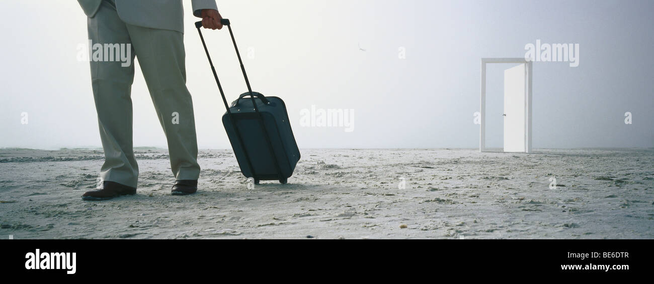 Man walking with rolling luggage on beach, open door in distance Stock Photo