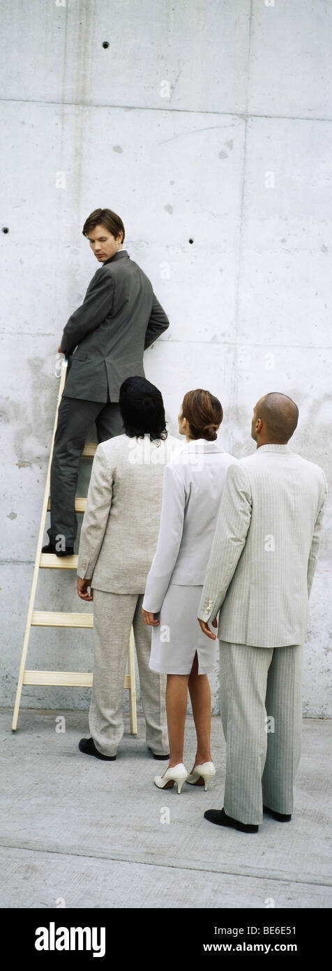 Businessman climbing ladder, looking over shoulder at professionals lined up behind him Stock Photo