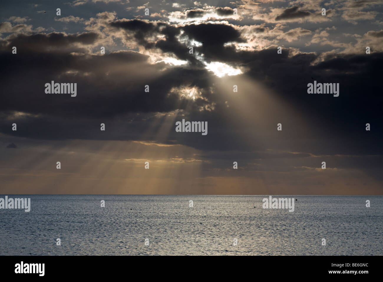 Sun bursting through clouds over a calm sea Stock Photo - Alamy