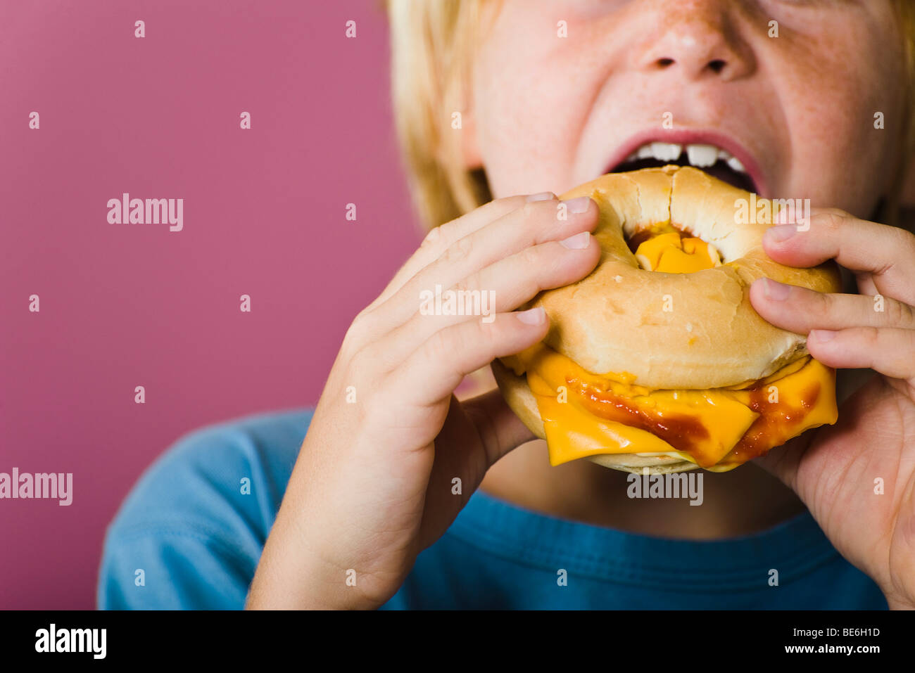 Boy eating bagel and cheese sandwich, cropped Stock Photo