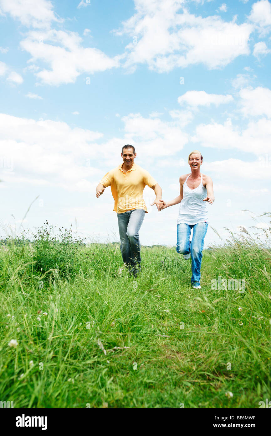 Couple running across a meadow, holding hands Stock Photo