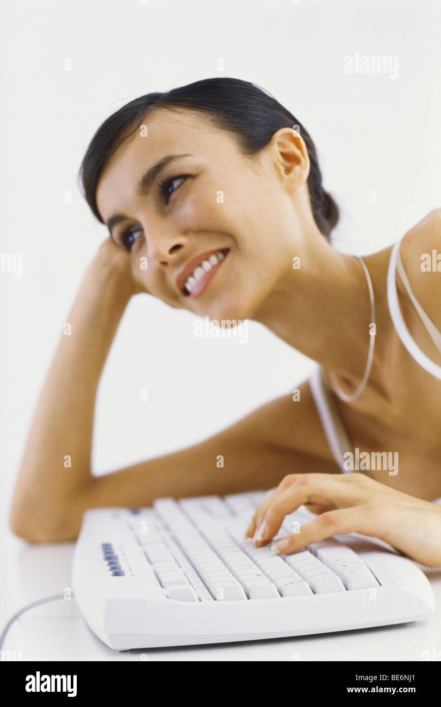 Woman leaning on elbow typing on keyboard, smiling Stock Photo