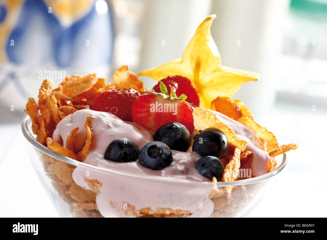 Fruit yoghurt in a glass bowl, corn flakes, blueberries, carambola