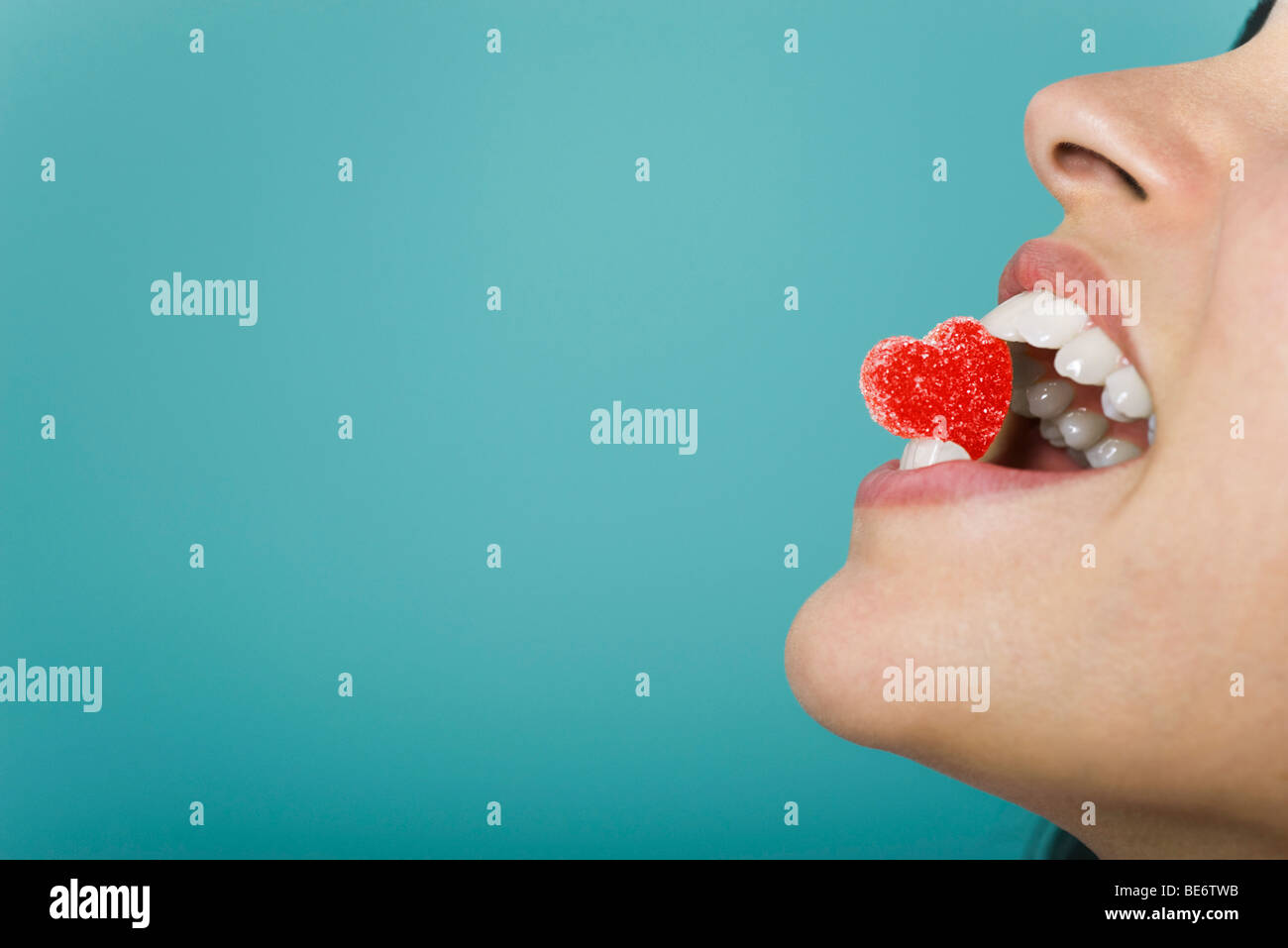 Woman holding heart-shaped candy between teeth, cropped Stock Photo