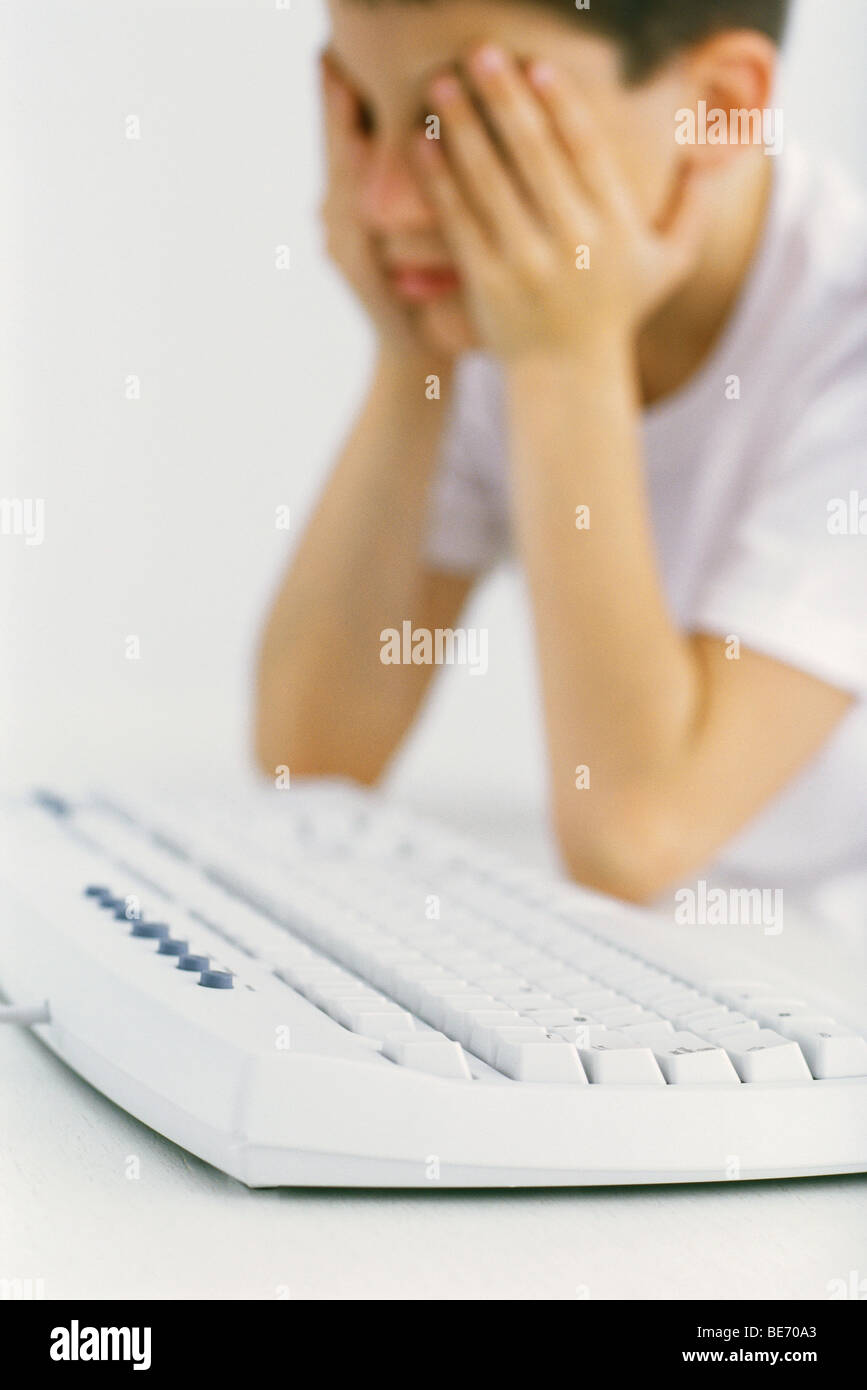 Boy at computer keyboard holding head Stock Photo