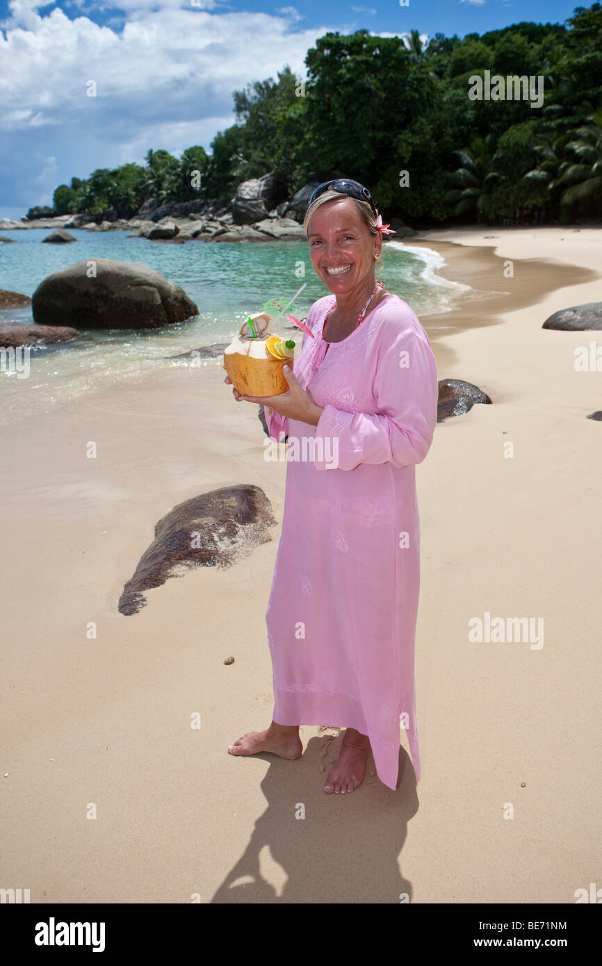 A woman in a pink tunic holding a decorated coconut filled with a drink, island Mahe, Seychelles, Indian Ocean, Africa Stock Photo