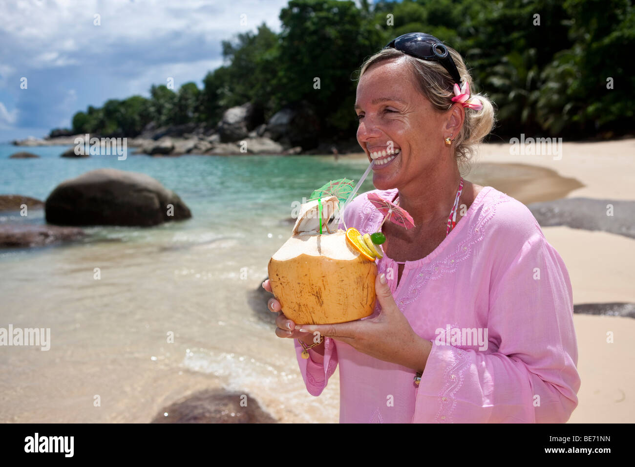 A woman in a pink tunic drinking from a decorated coconut filled with a drink, island Mahe, Seychelles, Indian Ocean, Africa Stock Photo