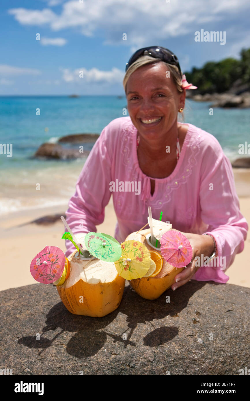 A woman in a pink tunic reaches for two decorated coconuts filled with drinks, island of Mahe, Seychelles, Indian Ocean, Africa Stock Photo