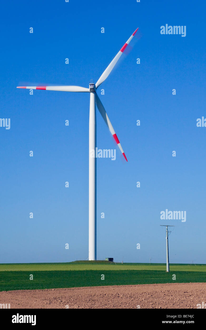 Wind turbine in front of the mast of a transmission line Stock Photo
