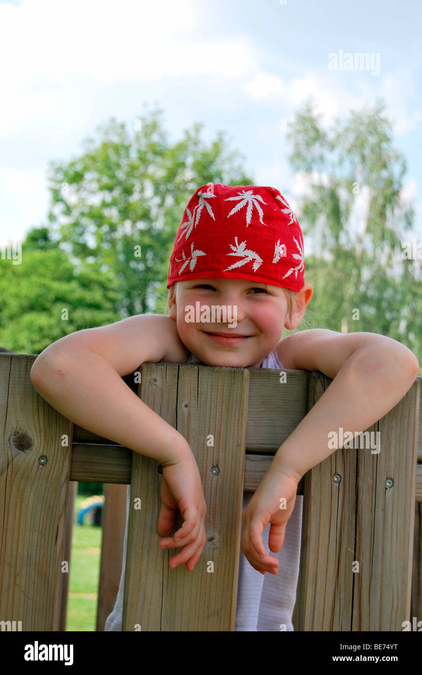Girl, 5, wearing a red headscarf hanging over a garden fence like a young rascal Stock Photo