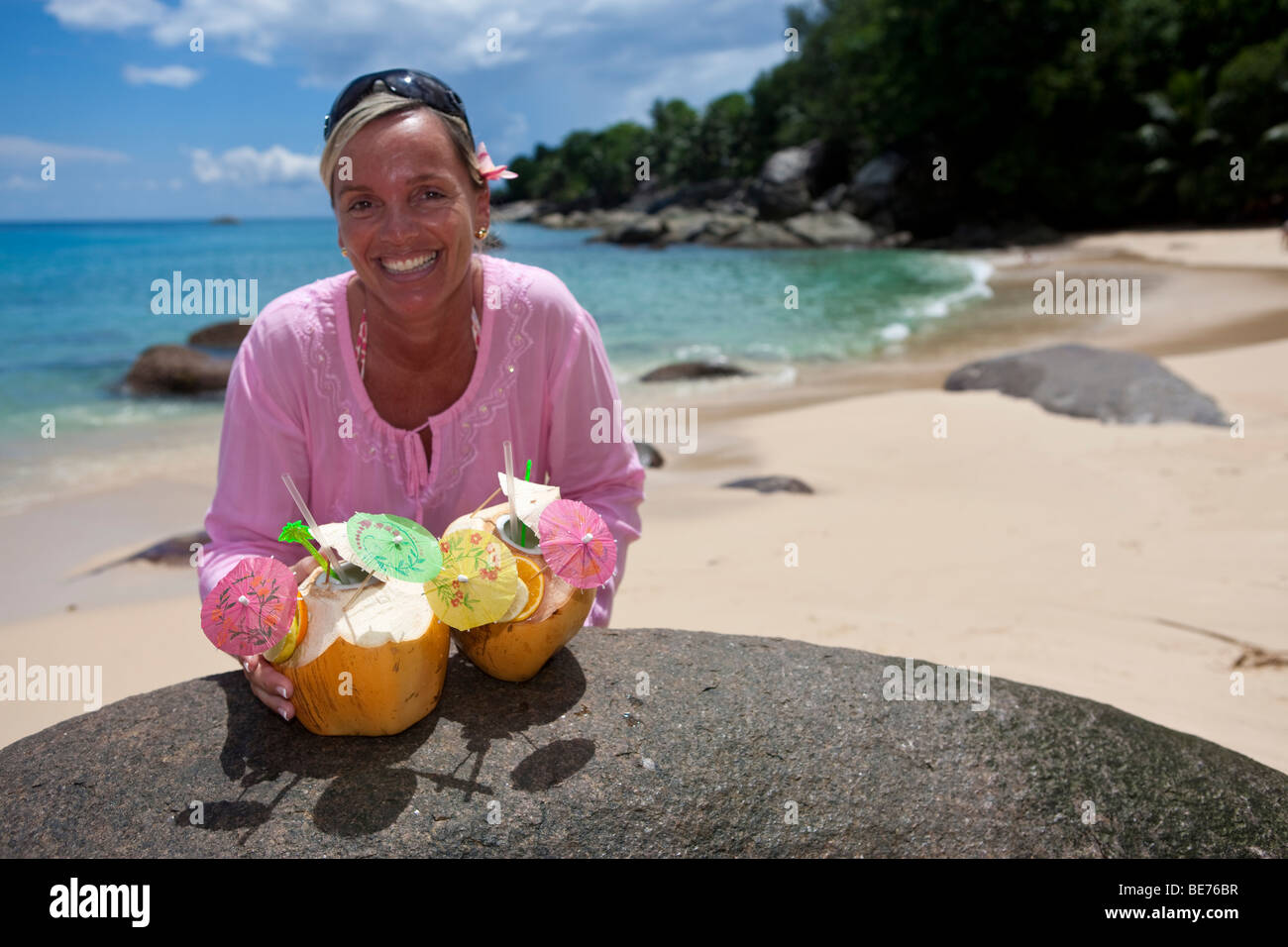 A woman in a pink tunic reaches for two decorated coconuts filled with drinks, island Mahe, Seychelles, Indian Ocean, Africa Stock Photo