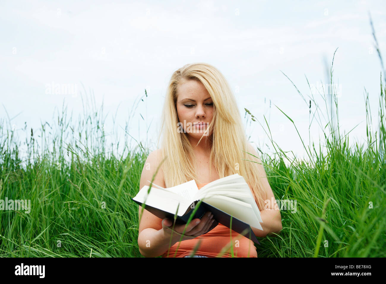 Young blonde woman sitting on a lawn, reading a book Stock Photo