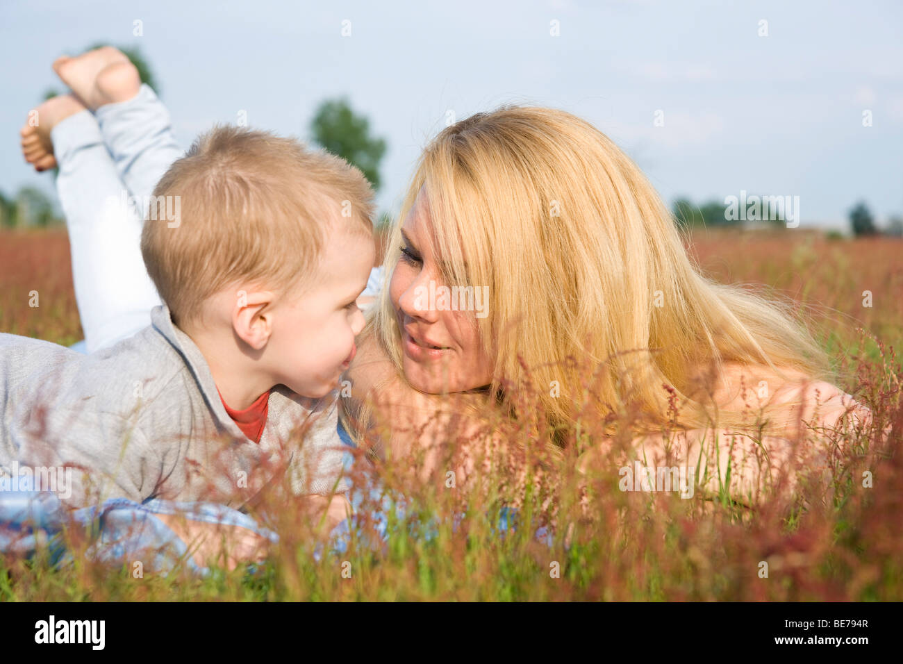 Young blonde woman lying in a meadow with her two-year-old son Stock Photo
