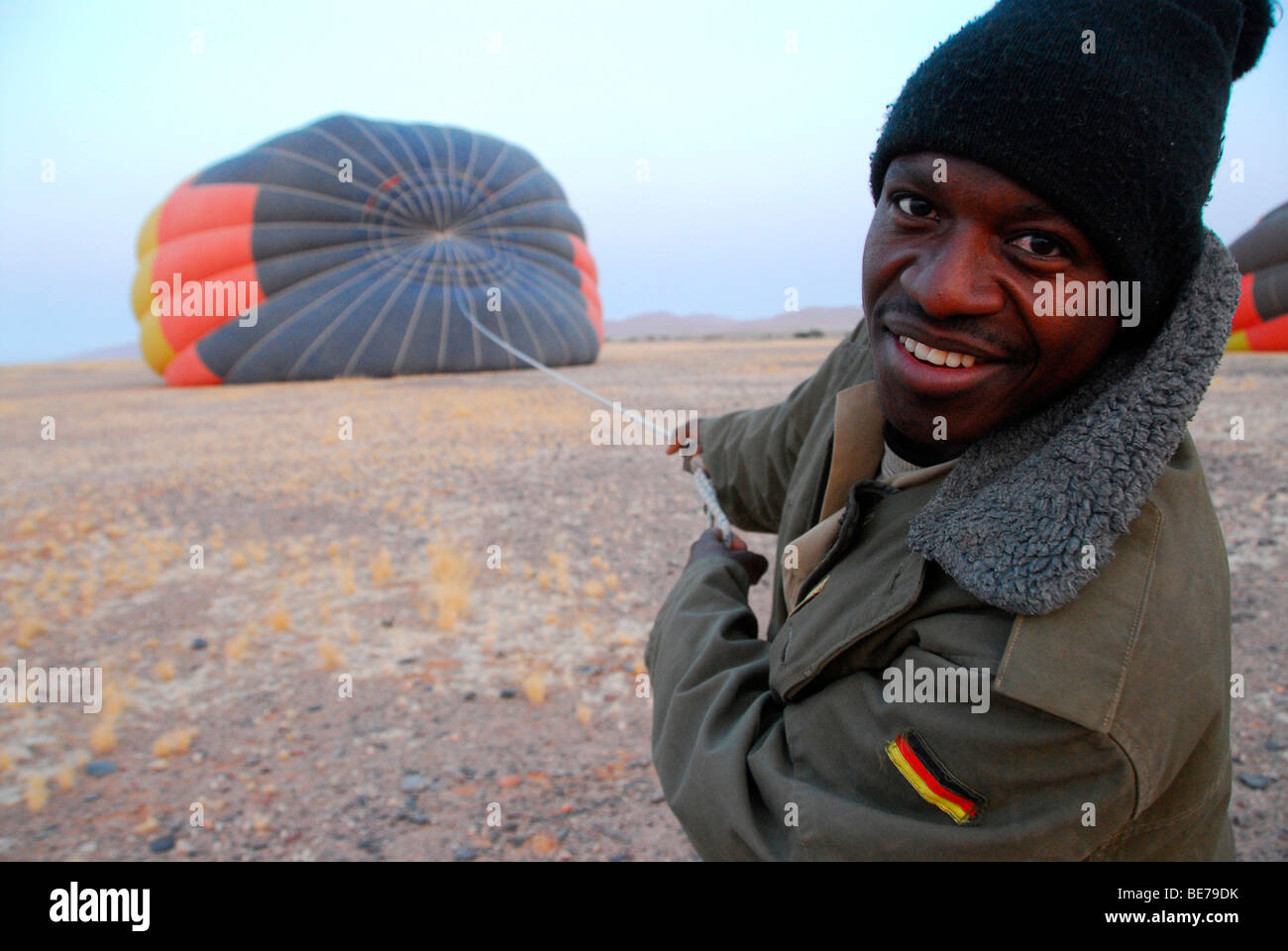 Native wearing a German army jacket helping to launch a balloon safari at dawn, Sossusvlei, Namibia, Africa Stock Photo