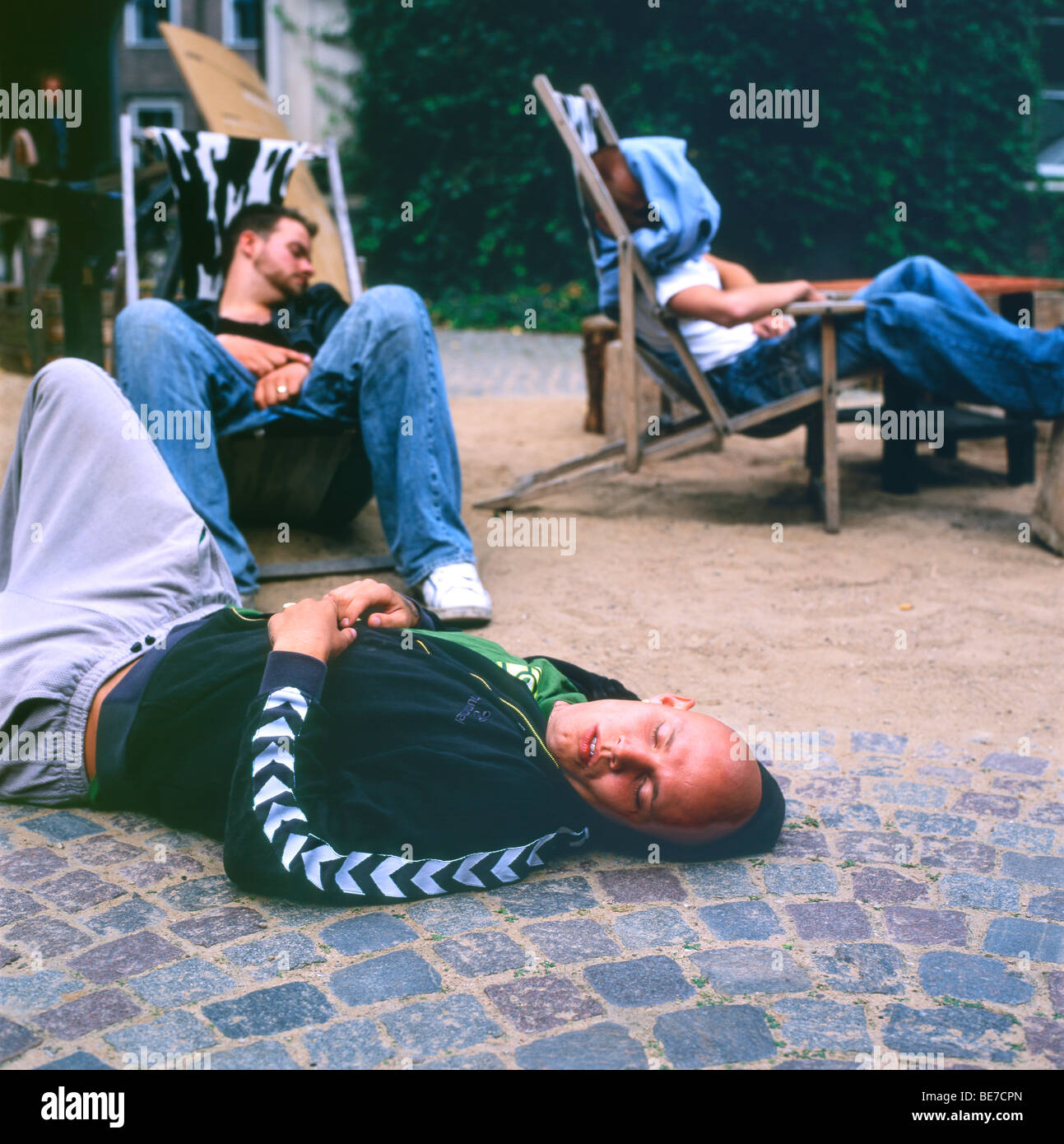Young men with hangovers lying in the street sleeping off the affects of alcohol Nyhavn in Copenhagen Denmark  KATHY DEWITT Stock Photo