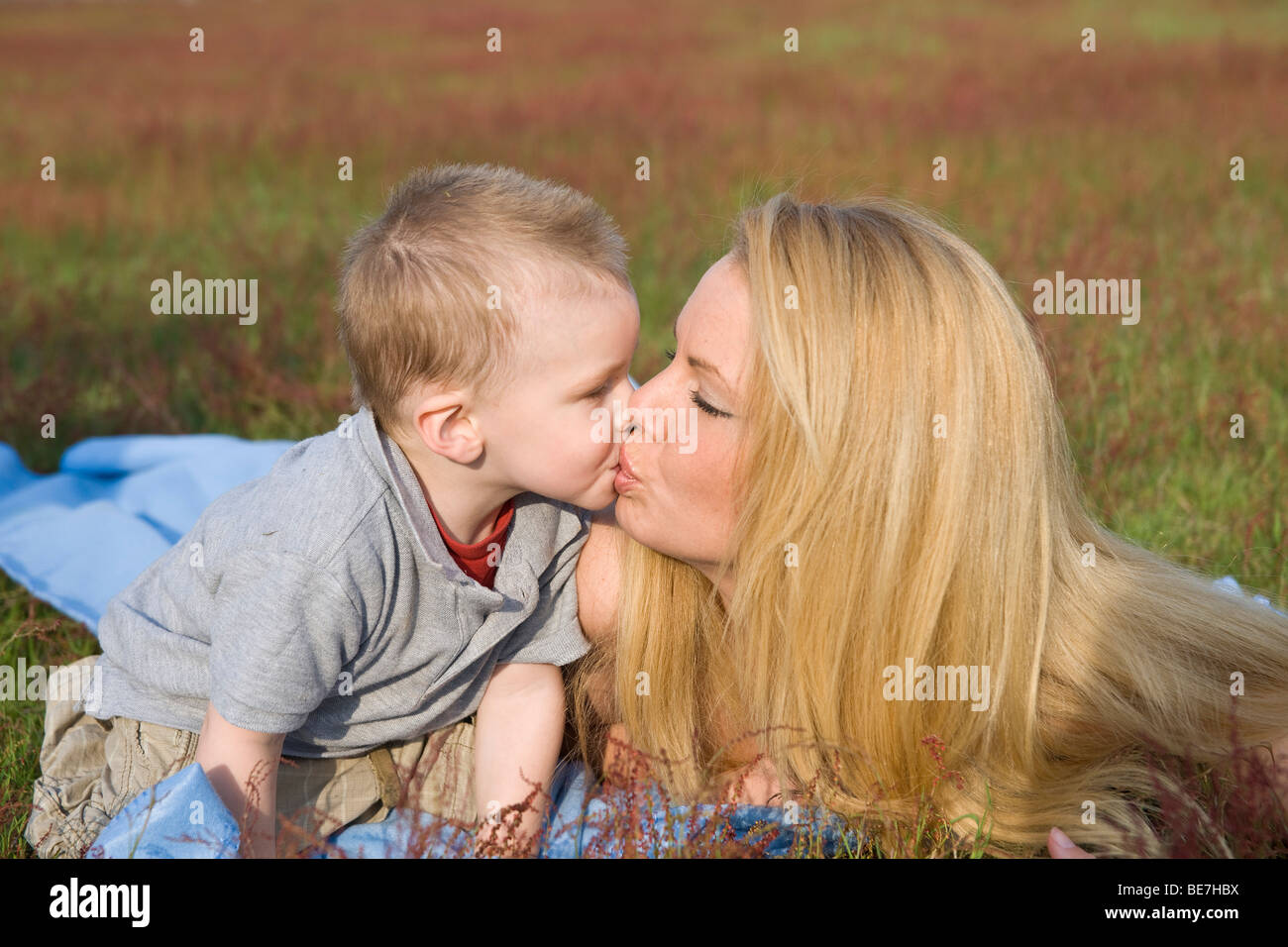 Young blonde woman kissing her son, in a meadow Stock Photo