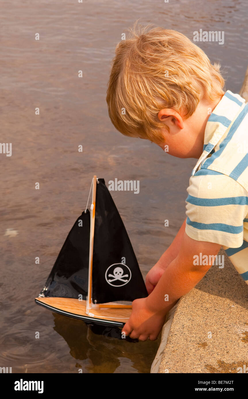 A small boy ( model released ) sailing his toy boat at the boating lake