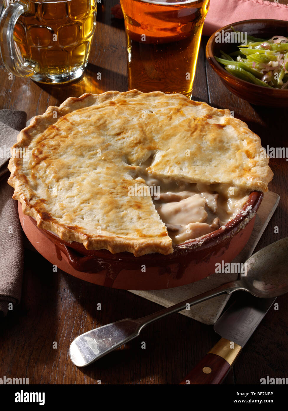 Whole family size chicken pie with runner beans and beer in a table setting Stock Photo