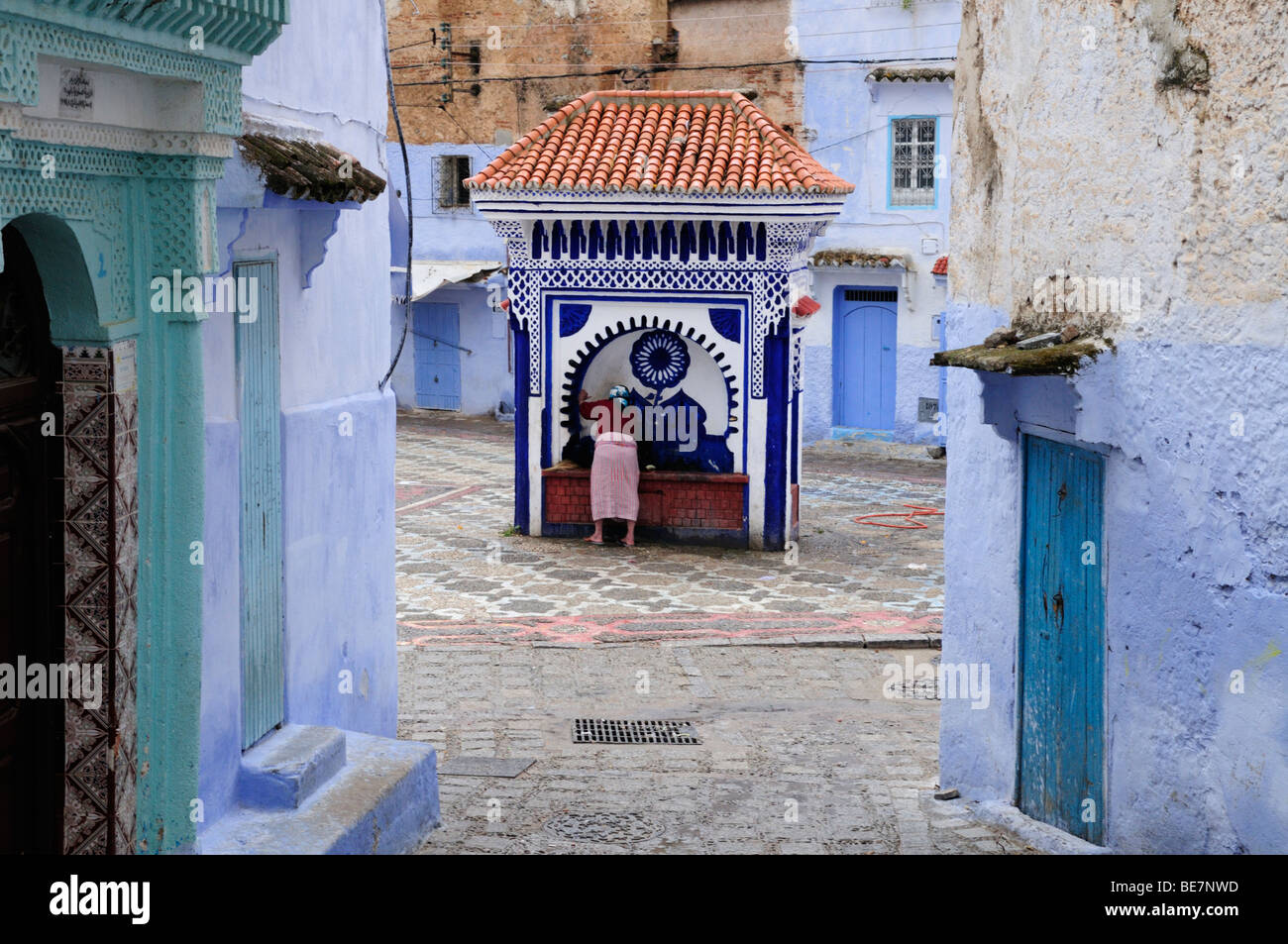 Morocco; Chefchaouen; Street Scene in the Medina showing a woman at one of the public water fountains Stock Photo