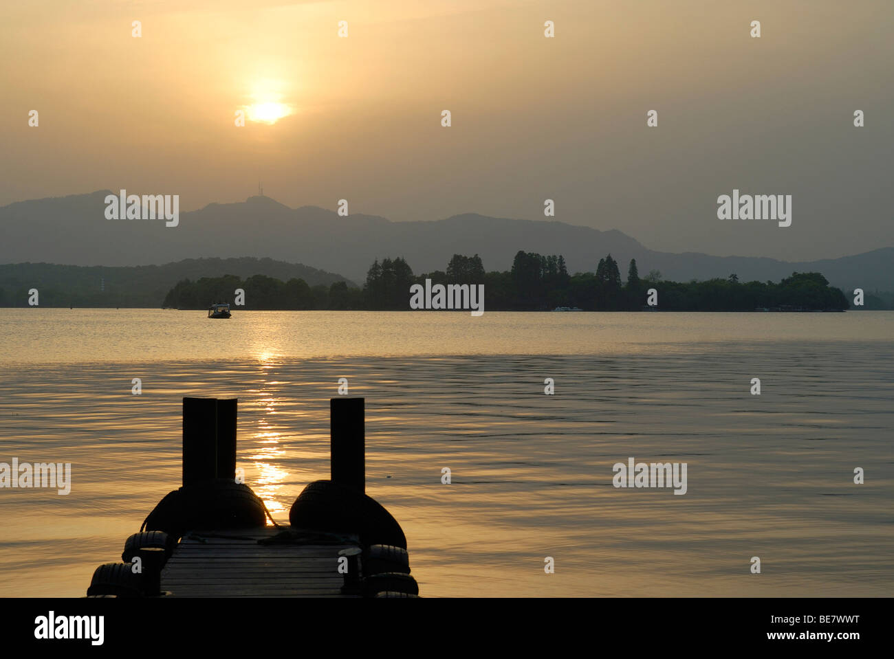 Evening sun with a wooden footbridge at West Lake, Chinese: Xi Hu, in front of a mountain backdrop and boat, Hangzhou, China, A Stock Photo