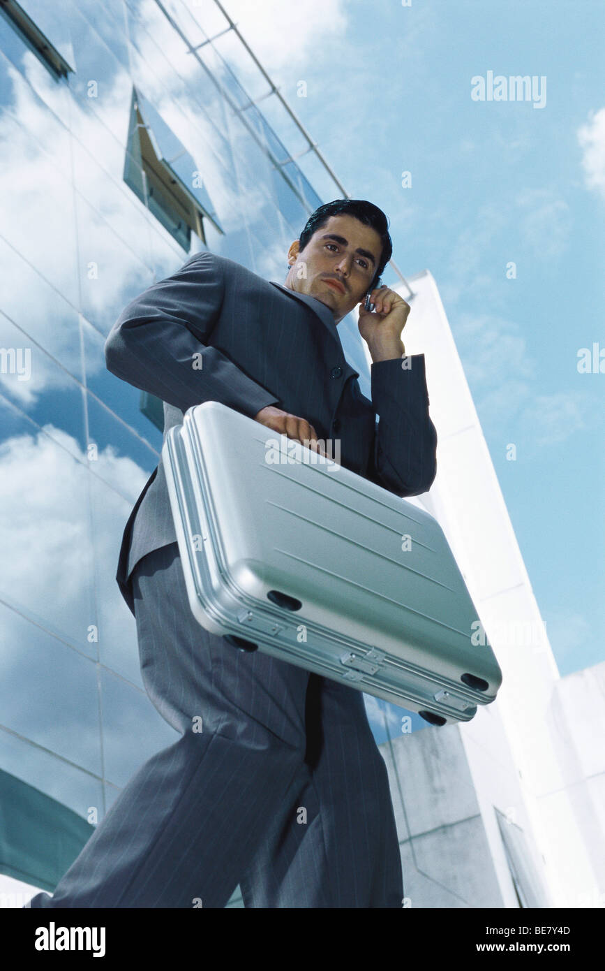 Businessman carrying briefcase using cell phone outside office building