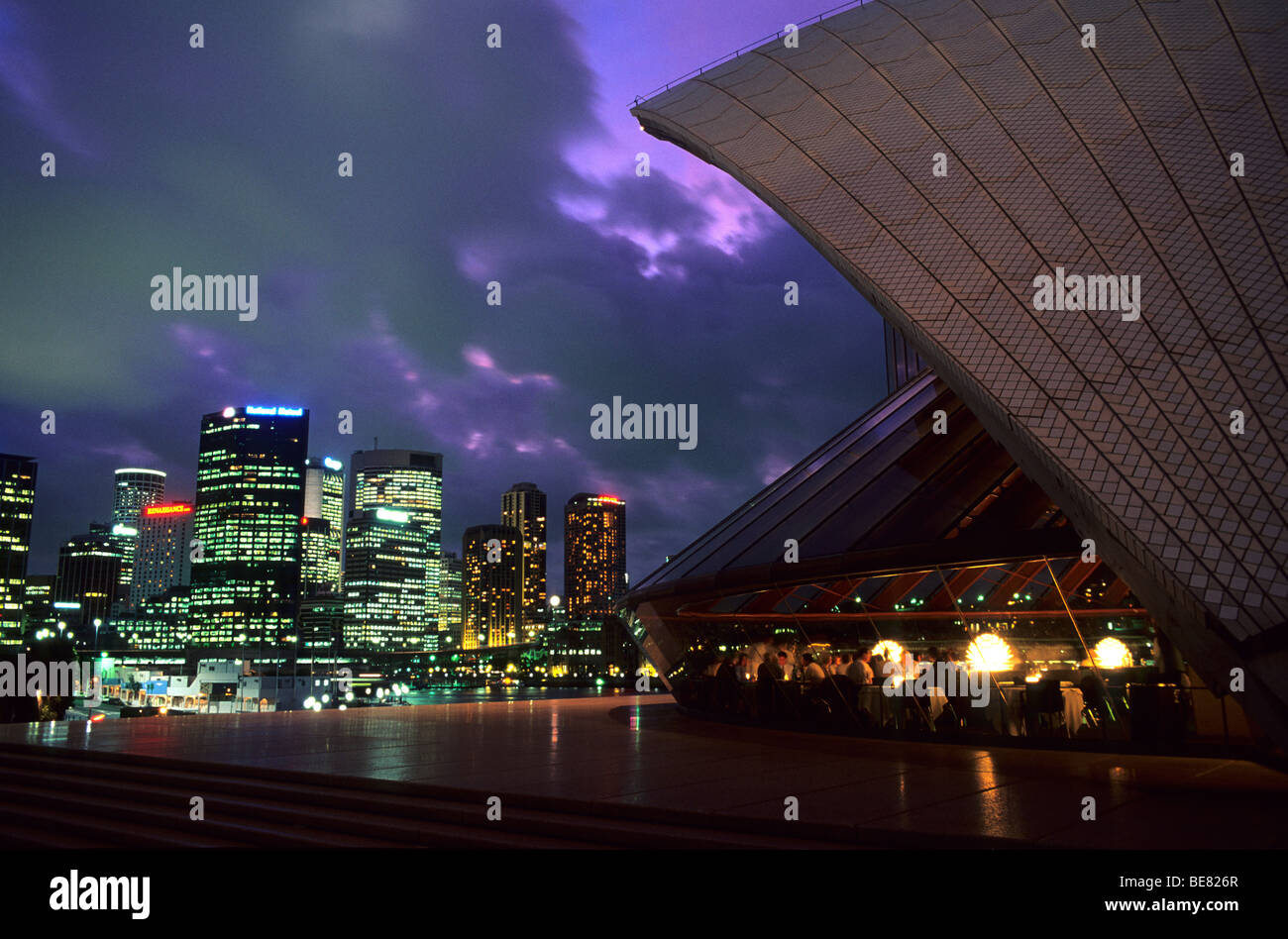 People inside the Bennelong Restaurant at the Opera House and illuminated high rise buildings, Sydney, New South Wales, Australi Stock Photo