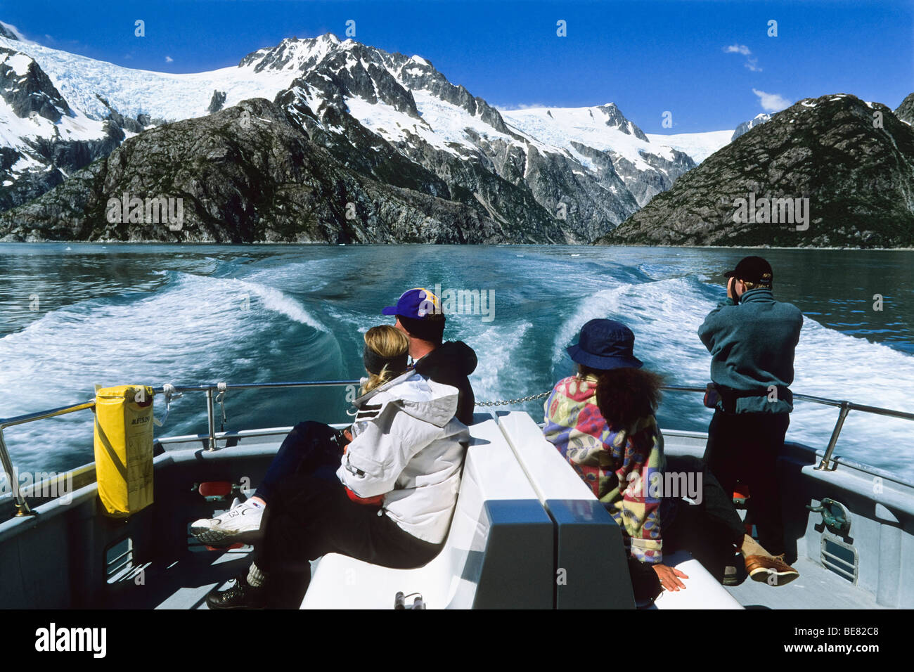 People sitting in the stern of an excursion boat, view at snow covered mountains, Inside Passage, Southeast Alaska, USA Stock Photo