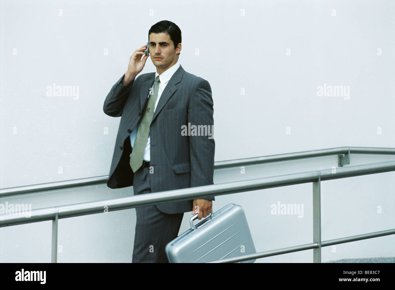 Businessman walking on sidewalk using cell phone, carrying briefcase