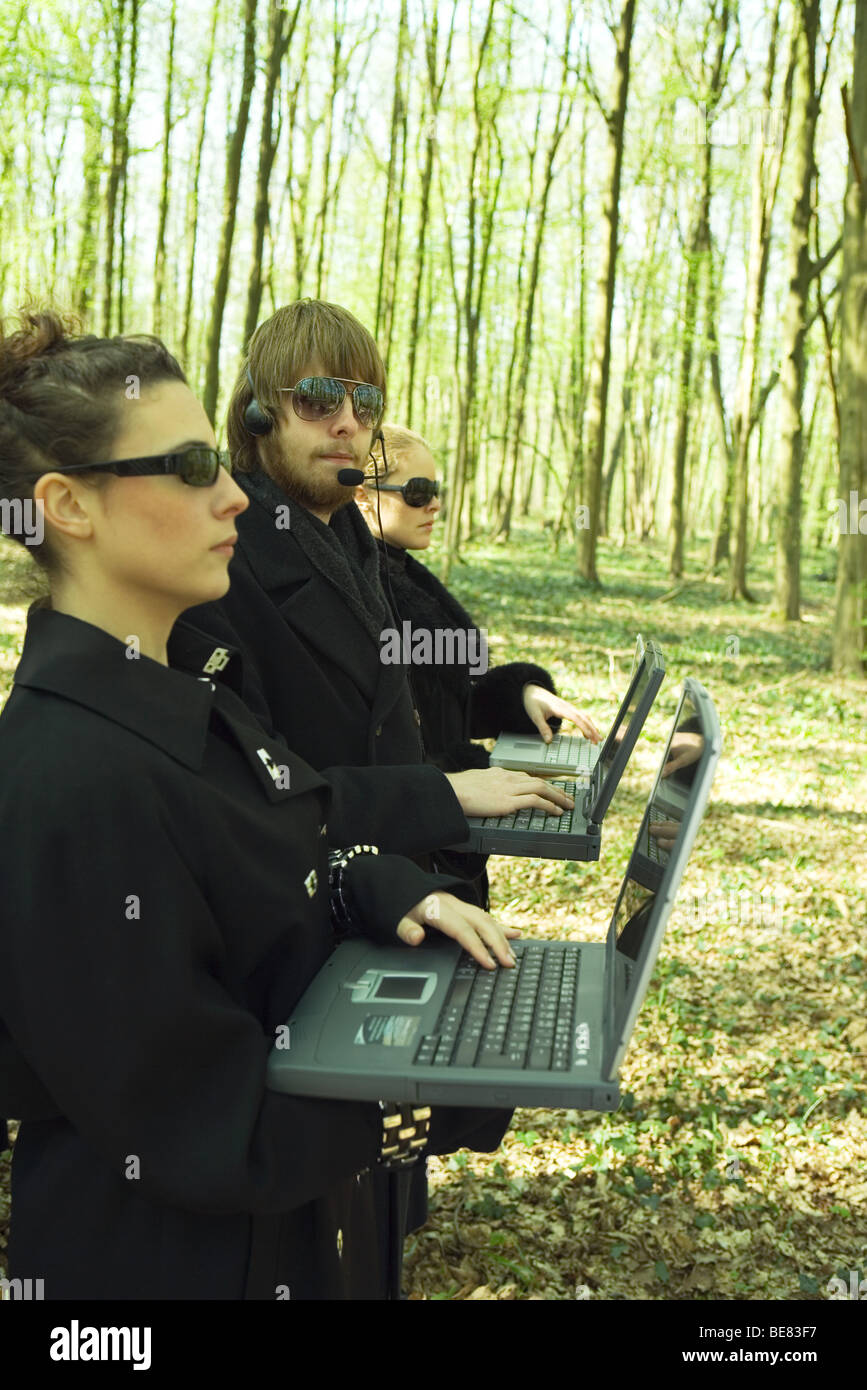 Man standing between two women in woods, looking at camera, all using laptop computers Stock Photo
