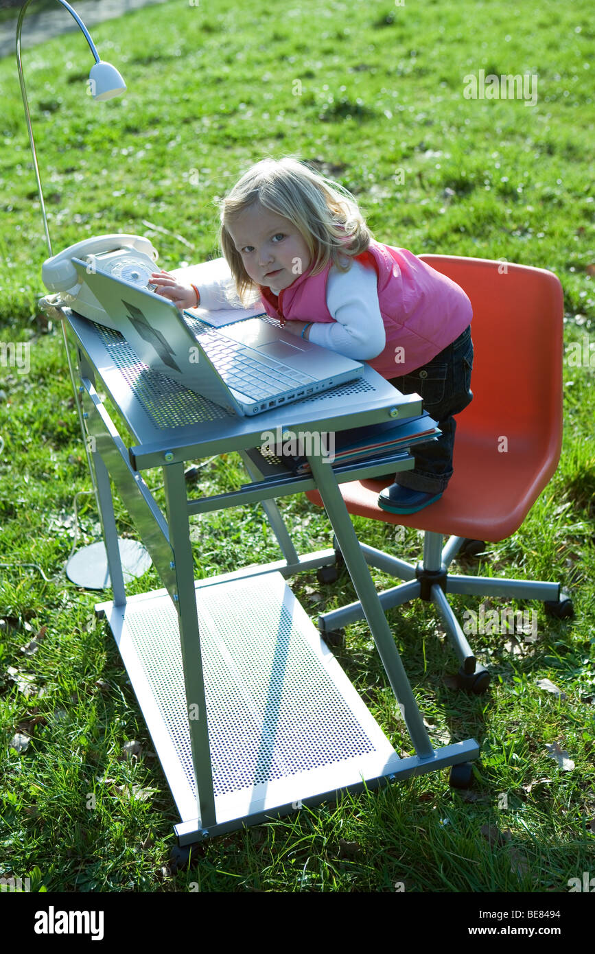 Little Girl Standing On Office Chair By Desk In Field Playing