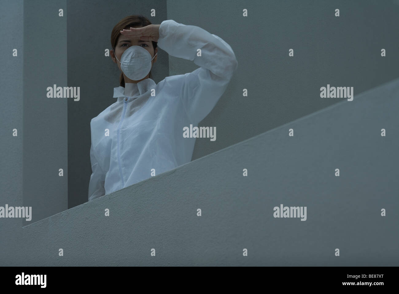 Woman in pollution mask and protective suit looking away, shading eyes Stock Photo
