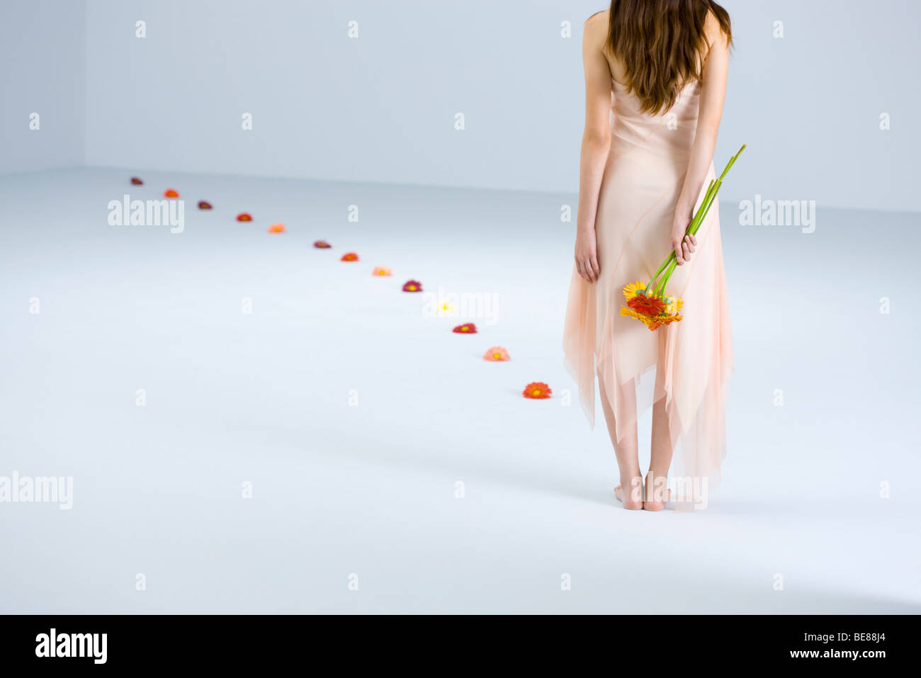 Woman holding bouquet behind back, path of flowers leading away from her, rear view Stock Photo