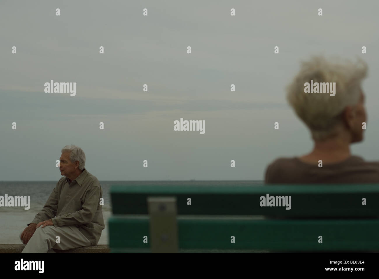 Senior man sitting on bench, looking away, senior woman in foreground Stock Photo
