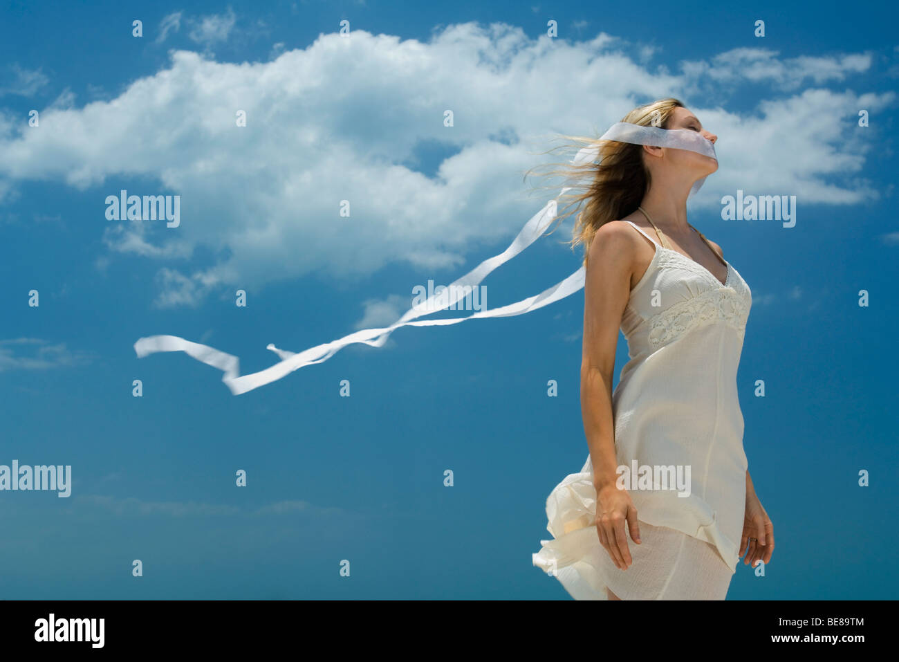 Woman with ribbon covering mouth, ends of ribbon blowing in the wind