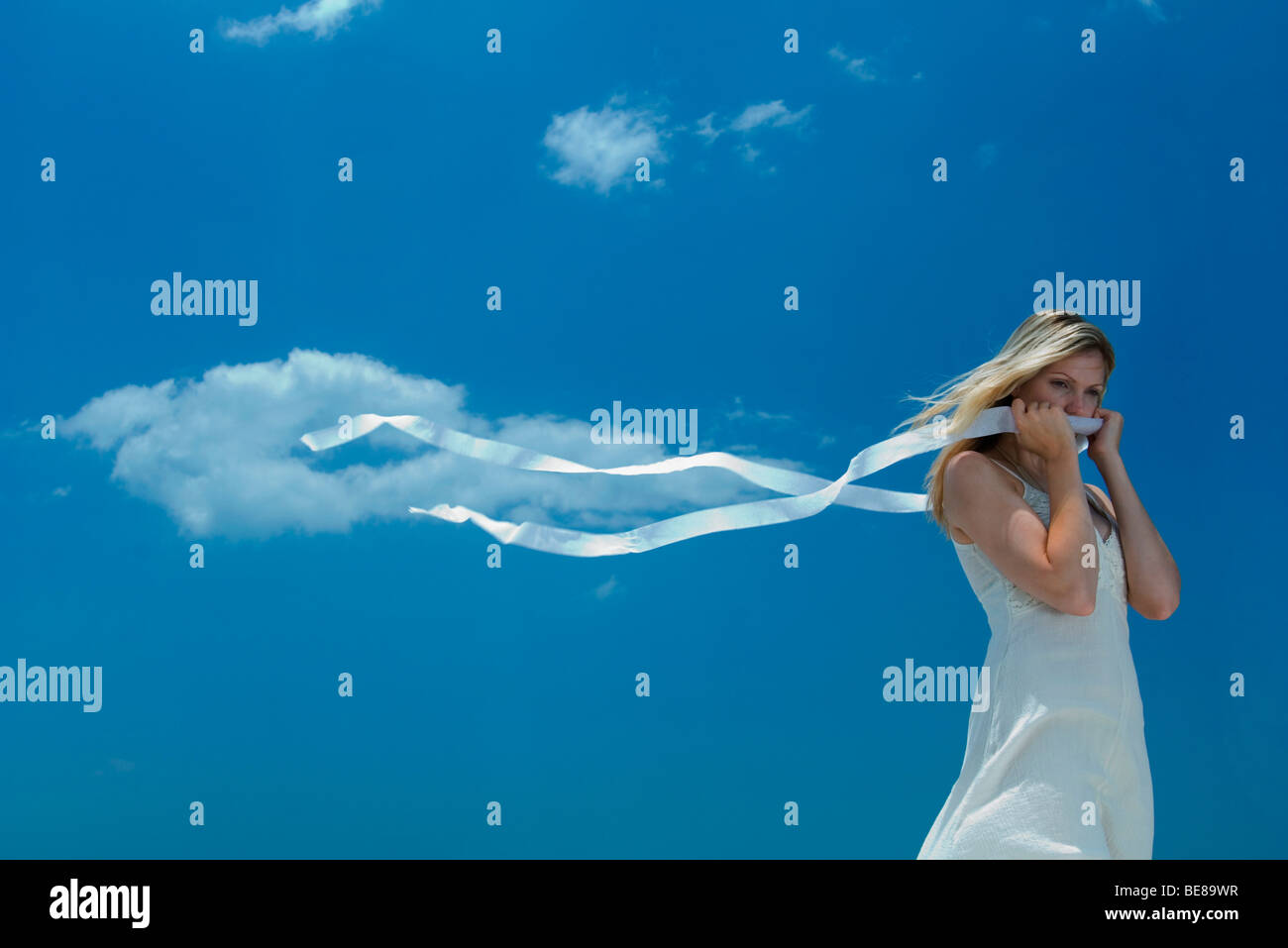 Woman holding ribbon covering mouth, ends of ribbon blowing in the wind