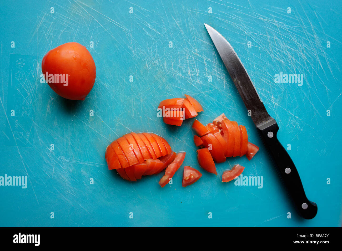 Freshly diced tomatoes on blue plastic chopping board with knife and cut marks. Stock Photo