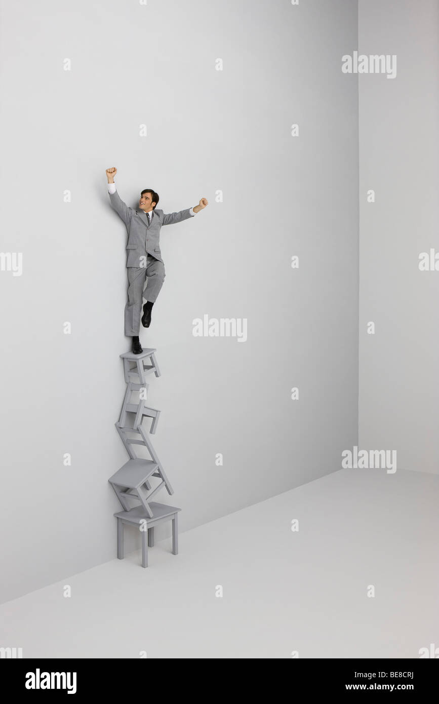 Businessman standing with arms raised atop stack of chairs Stock Photo