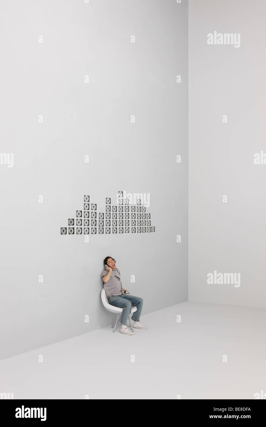 Man singing along with music playing on MP3 player, CD cases arranged in pattern on wall Stock Photo