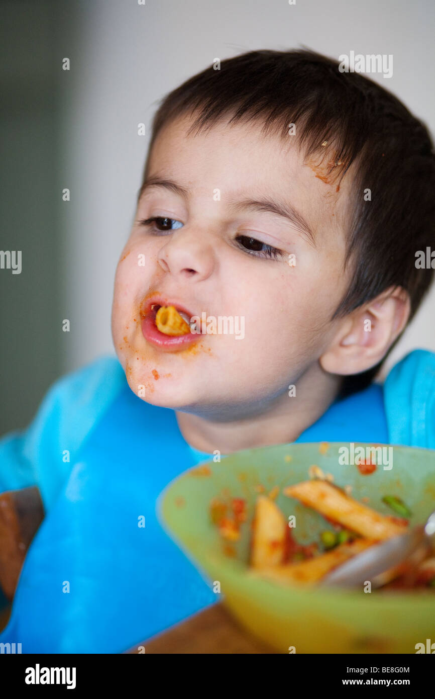 3 year old boy eating pasta at a dinner table Stock Photo