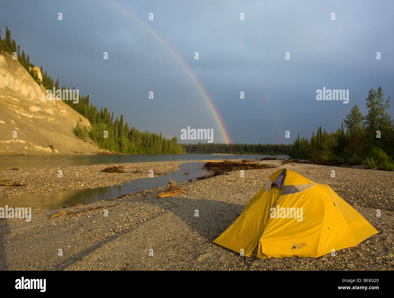 Tent on a gravel bar, rainbow behind, upper Liard River, Yukon Territory, Canada Stock Photo