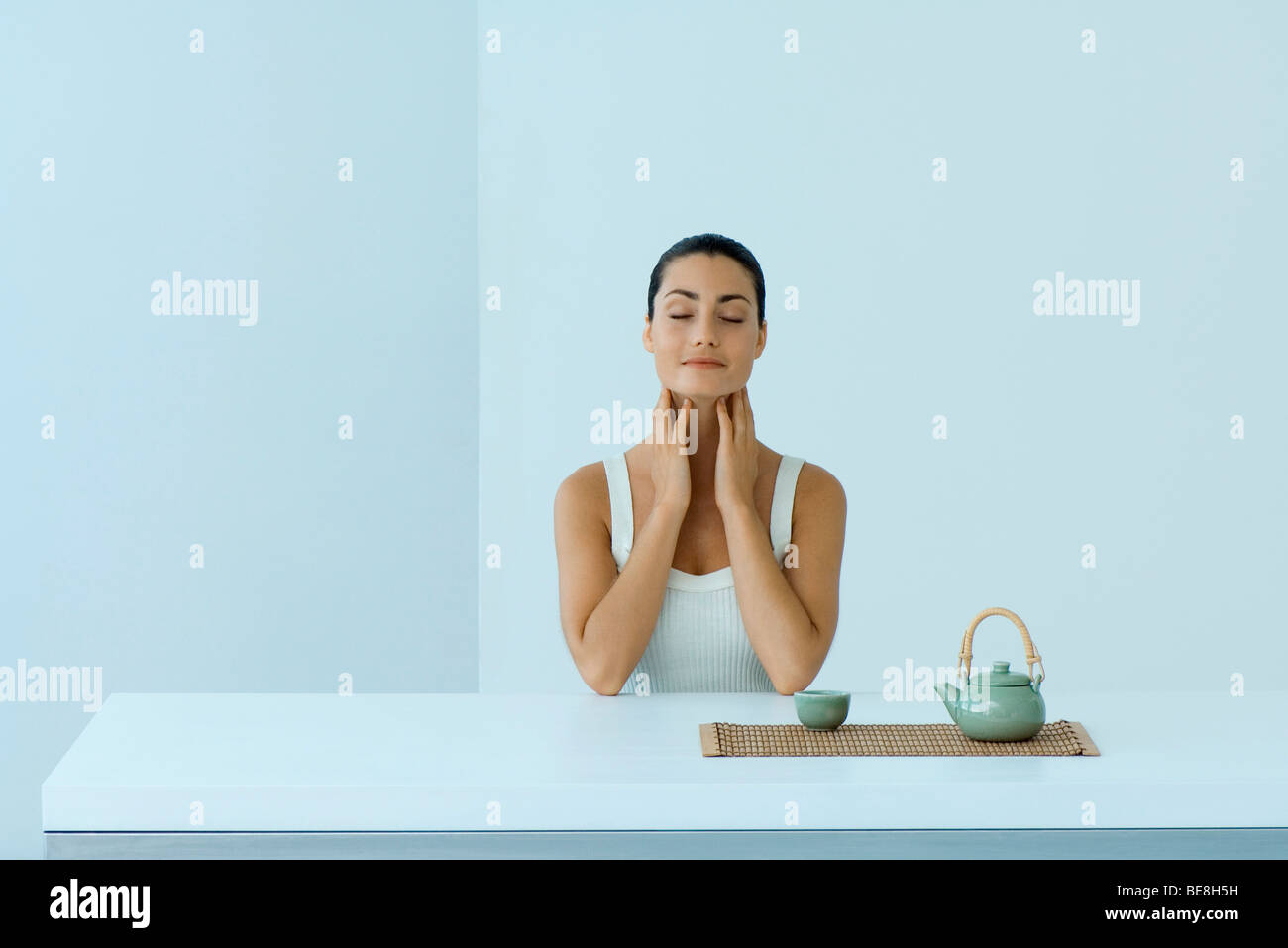 Woman sitting with teapot, holding neck, eyes closed Stock Photo