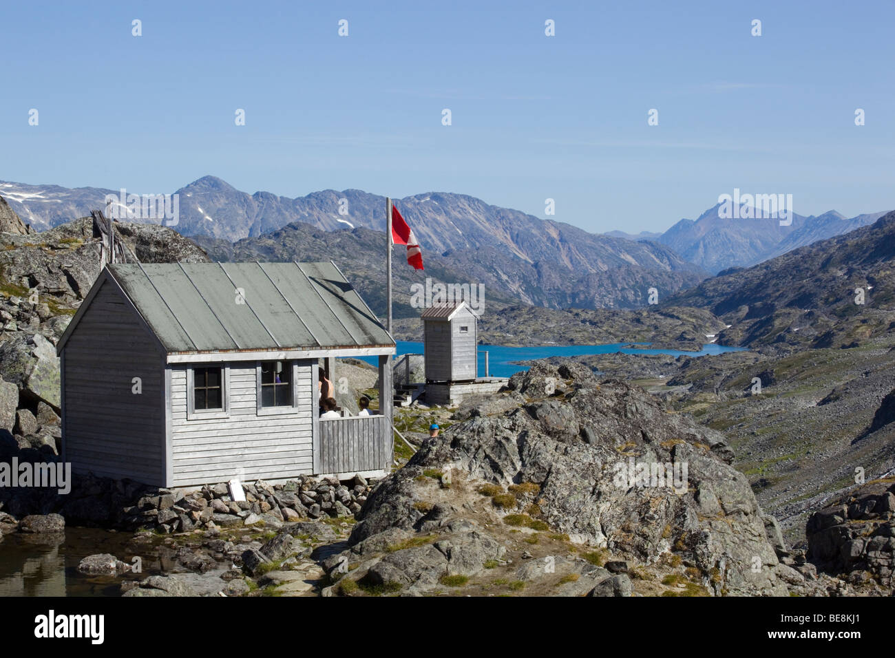 Shelter and outhouse on summit of historic Chilkoot Trail, Chilkoot Pass, Crater Lake behind, Canadian flag, Yukon Territory, B Stock Photo