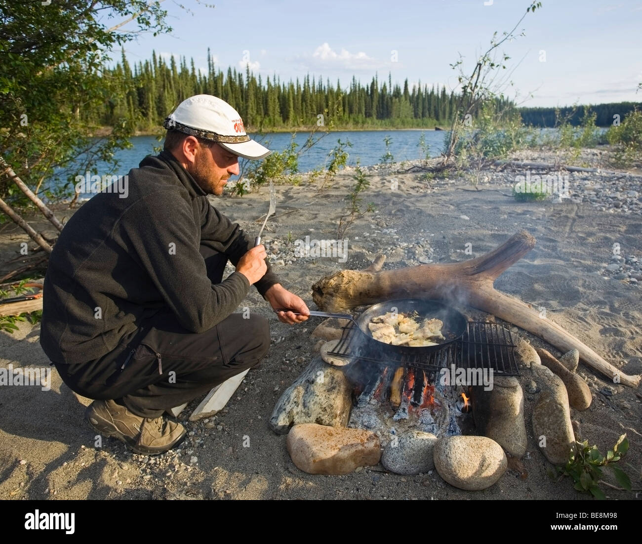 Man cooking, frying fish fillets in a pan on a camp fire, upper Liard